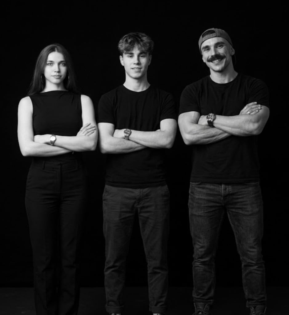 Studio portrait of the Lemmacorp team — one woman and two men on a black background